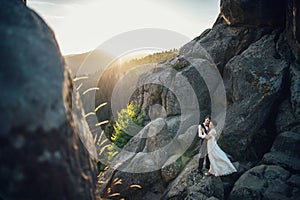 Romantic newlywed couple posing in sunset lights on majestic roc