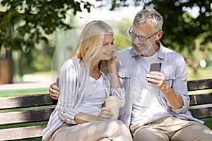 Romantic Older Couple With Smartphone Relaxing On Bench In Summer Park