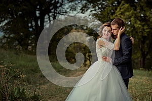 Romantic outdoor portrait. Stylish attractive newlywed couple is hugging and gorgeous bride is softly stroking the groom