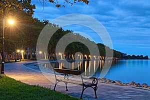 Romantic and peaceful scene. Empty bench illuminated by lamppost. Morning landscape view of Lake Balaton and Plane tree alley