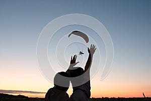Romantic photo, young couple standing together and waving hands to the hand glider that flying in the sky at sunset