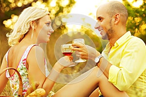 Romantic picnic concept. Portrait of a young loving couple in trendy casual clothes drinking red wine and enjoying each other.