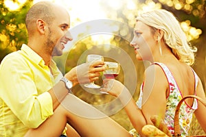 Romantic picnic concept. Portrait of a young loving couple in trendy casual clothes drinking red wine and enjoying each other.