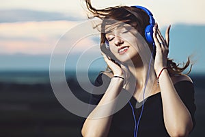 Romantic portrait of a beautiful girl in headphones, young woman listening to music on the nature in the field