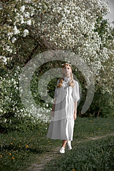 Romantic portrait of a girl in the park near a blooming apple tree. Natural cosmetics. Natural beauty of a woman in a white dress