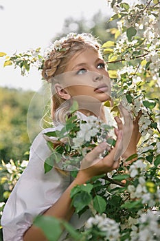 Romantic portrait of a girl in the park near a blooming apple tree. Natural cosmetics. Natural beauty of a woman in a white dress