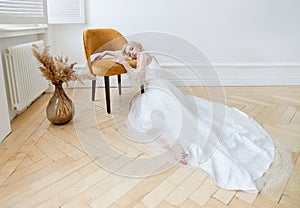 Romantic portrait of a woman on the floor in a beautiful long white dress. The girl is blonde with blue eyes and beautiful makeup