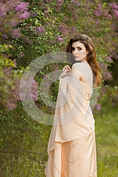 Romantic portrait of young beautiful girl standing in spring lilac garden