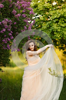 Romantic portrait of young beautiful girl standing in spring lilac garden