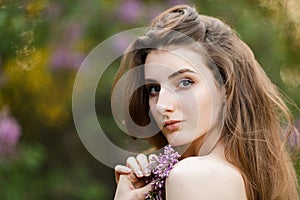 Romantic portrait of young beautiful girl standing in spring lilac garden