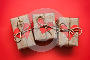 Romantic presents set. Gift boxes wrapped in brown craft paper and tie hemp string. Carton hearts. Red solid background.