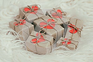Romantic presents set. Gift boxes wrapped in brown craft paper and tie hemp string. Carton hearts. White fur background.