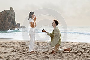 Romantic proposal on the seashore. Loving young man with engagement ring making proposal to happy woman on beach