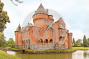 A romantic red castle with a tall tower surrounded by a moat