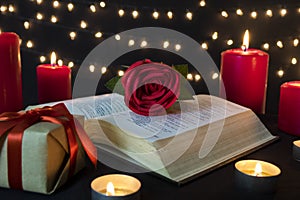 Romantic red rose on open book with gift box and candles in bokeh lights at night
