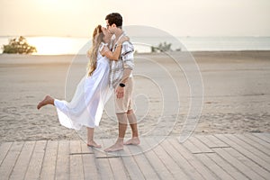 Romantic scene of beautiful young pregnant couple embraced on the beach at sunset.