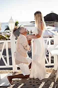 Romantic scene of a happy man making proposal to his beautiful woman on the beach.  Multiethnic couple