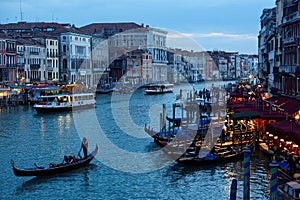 Romantic scenery of tourists riding in a gondola on Grand Canal at sunset, with ferry boats parking by restaurants & bars