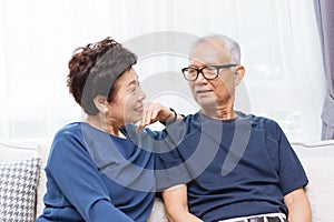 Romantic senior Asian couple laughing and sitting on sofa at home.
