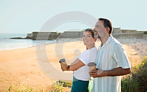 Romantic senior couple with coffee having summer vacation by coastline