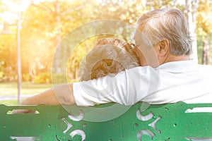 Romantic senior couple. Grandfather embracing, kissing grandmother. Lovely elderly couple sitting on bench at park. Elderly man an