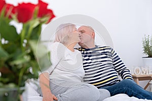 Romantic senior couple kissing on bed. bouquet of roses