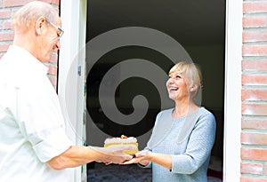 Romantic senior man giving a present cake to his wife through the window