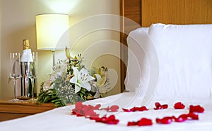 Romantic setup with honeymoon bed with focus on the bouquet and champagne bottle and flute