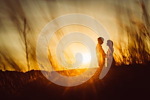 Romantic silhouette couple standing and kissing on background summer meadow sunset