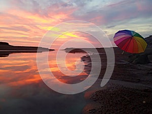 Romantic sky, dramatic colorful sunset over the sea background with rainbow umbrella.