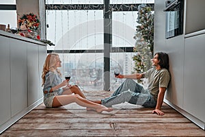 Romantic smiling couple sit on warm kitchen floor talking holding glasses having fun together, happy friendly husband and wife