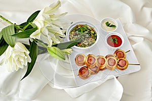 Romantic snack setting with pigs in blankets on skewers and white lilies