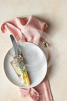 Romantic or spring table setting. Knife and fork, little pink flowers and linen napkin on a plate, light concrete background. Flat