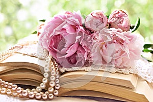 Romantic still life with pink peonies lying on old books in the garden
