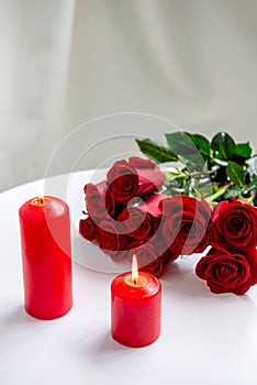 Romantic still life, there are two red burning candles and a bouquet of roses on the table