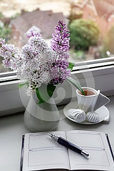 Romantic still life on the windowsill blue flowers in a vase, a cup of coffee and a notebook for notes, spring time