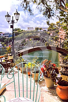 Romantic style coffee shop. Charming garden of cafe with stylish decor. Bridge over the lake, metalwork chair, lantern and plants.