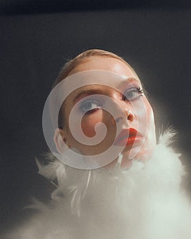 Romantic stylish young female model with white feathers collar, long lashes red lips, close up studio portrait