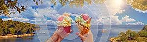 Romantic summer landscape panorama of a couple with bright sweet ice cream of different flavors in the hands and sea on background