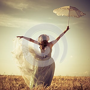 Romantic summer outdoors fairy: beautiful blond young woman having fun wearing long light dress and holding white lace umbrella