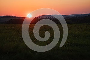 romantic sunset behind a hill in front of a meadow