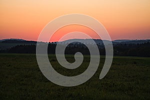 romantic sunset behind a hill in front of a meadow