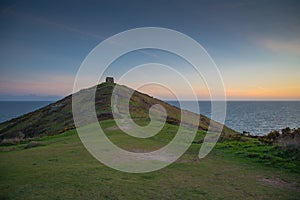 Romantic sunset on Cornish coast with lonelly chapel on cliff.