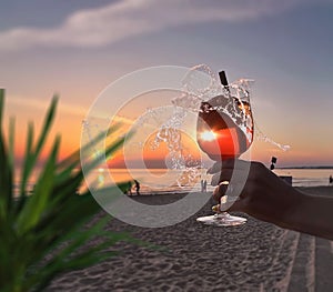 Romantic sunset Glass of orange limonade  tropical plant shadow  in young woman hand on front beach and sea on sky nature