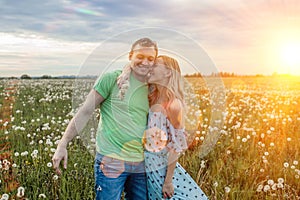 Romantic sunset photo of a happy couple hugging in a field with dandelions