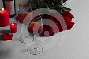 Romantic table setting with glasses of red wine, rose flowers and burning candles, space for text