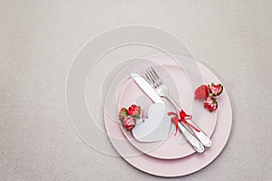 Romantic table setting on light stone concrete background. Valentine`s day or Wedding card template. Paper heart, flowers, cutler
