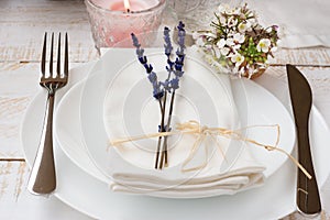 Romantic table setting, wedding, lavender, white small flowers, plates, napkin, lit candle, wood table, outdoors