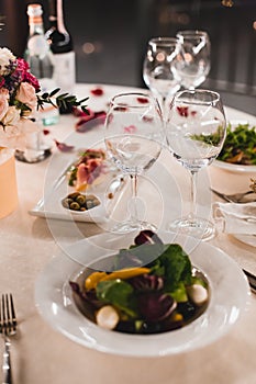 Romantic table setting with wine, beautiful flowers in box, empty glasses, rose petals and candles