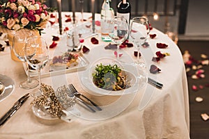 Romantic table setting with wine, beautiful flowers in box, empty glasses, rose petals and candles